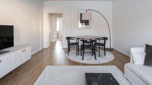 A modern living room with a flat-screen TV, a dining table with chairs, a white sofa, and a floor lamp. - Bright & Cozy 1BR Home near Downtown (Lahti)