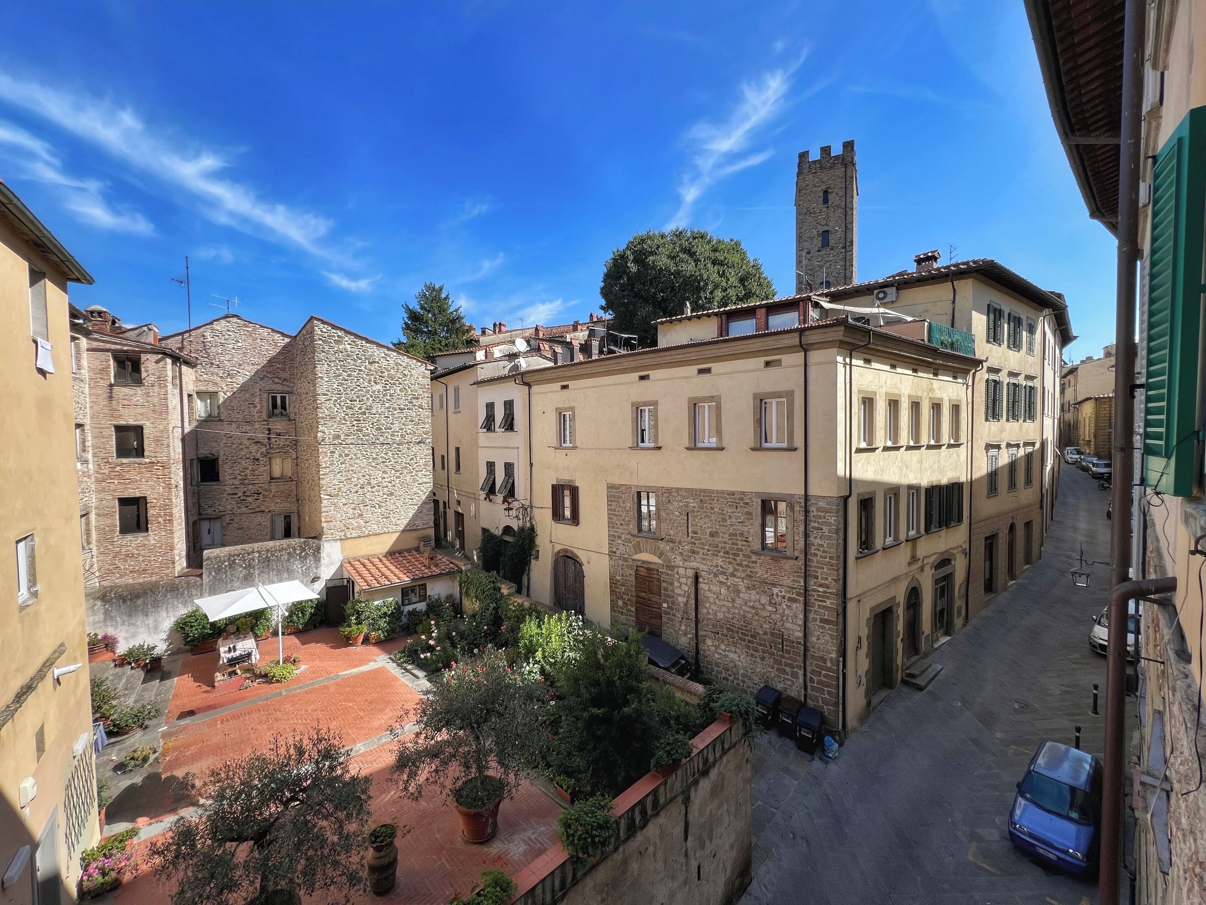 A narrow street with historic buildings, a tower, and a courtyard with potted plants.