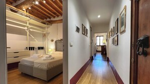 Un corridoio d'albergo con pavimento in legno, un letto con asciugamani ordinatamente piegati, soffitto in legno e una galleria con quadri appesi alle pareti.
