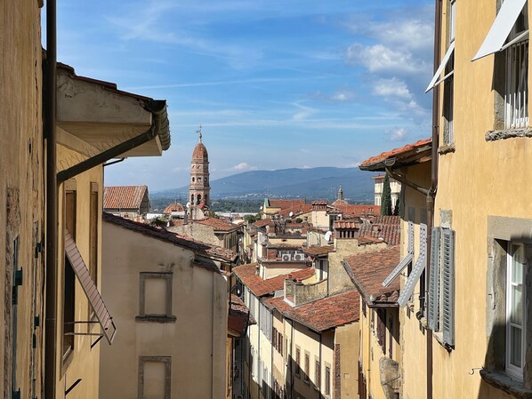 A narrow street with buildings featuring red-tiled roofs and a prominent tower in the background. - Aurora Guests House - One Bedroom Apartment, Sleeps 4 (Arezzo)