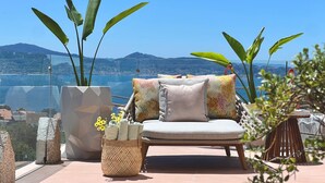 A balcony with a lounge chair, potted plants, and a view of a coastal landscape. - Aldea Calma (Sanxenxo)