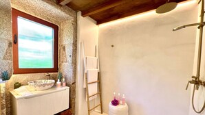 A bathroom with a stone wall, a window, a bathtub, a towel rack, and toiletries on the counter. - Aldea Calma (Sanxenxo)
