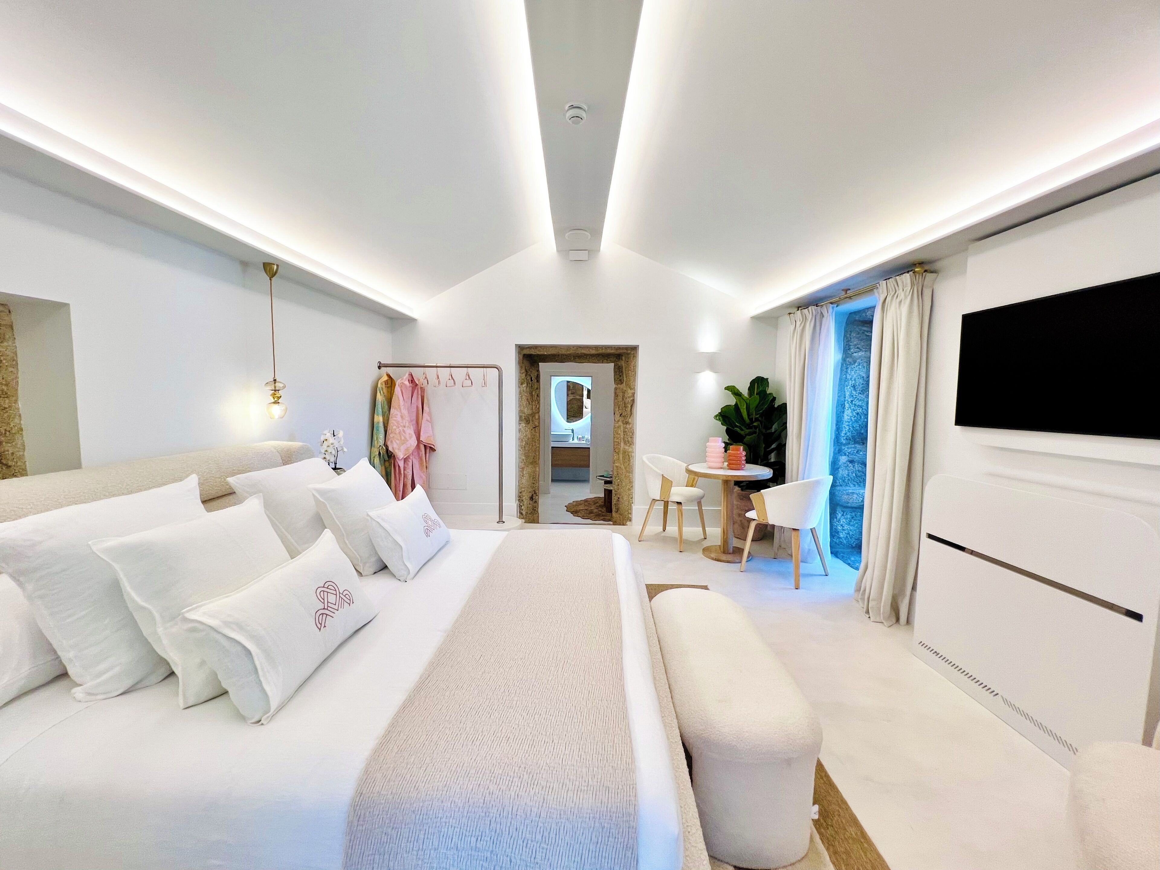 Un dormitorio moderno con una cama grande, mesitas de noche, un televisor y un baño visible a través de una puerta abierta.