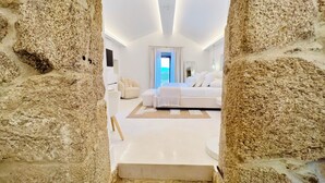 A modern bedroom with a large bed, a sitting area, and a view of the outdoors through a window. - Aldea Calma (Sanxenxo)