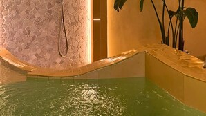 A spa area with a stone wall, a shower, a clock, and a plant. - Aldea Calma (Sanxenxo)