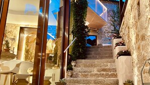 A modern hotel interior with a stone staircase leading to a balcony, glass doors, and indoor seating area. - Aldea Calma (Sanxenxo)