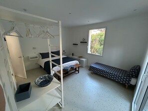 Quarto com beliche, uma cama de solteiro, mesa de cabeceira, janela com vista e um pequeno espaço de estar.