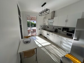Una cocina moderna con armarios blancos, un refrigerador de acero inoxidable y una zona de comedor con mesa y sillas.
