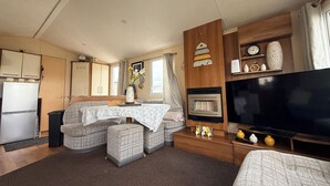 A compact living space with a kitchenette, a dining area, a sofa set, a television, and a fireplace. - Cala Gran Holiday Park - Holiday Accommodation 10830 (Fleetwood)