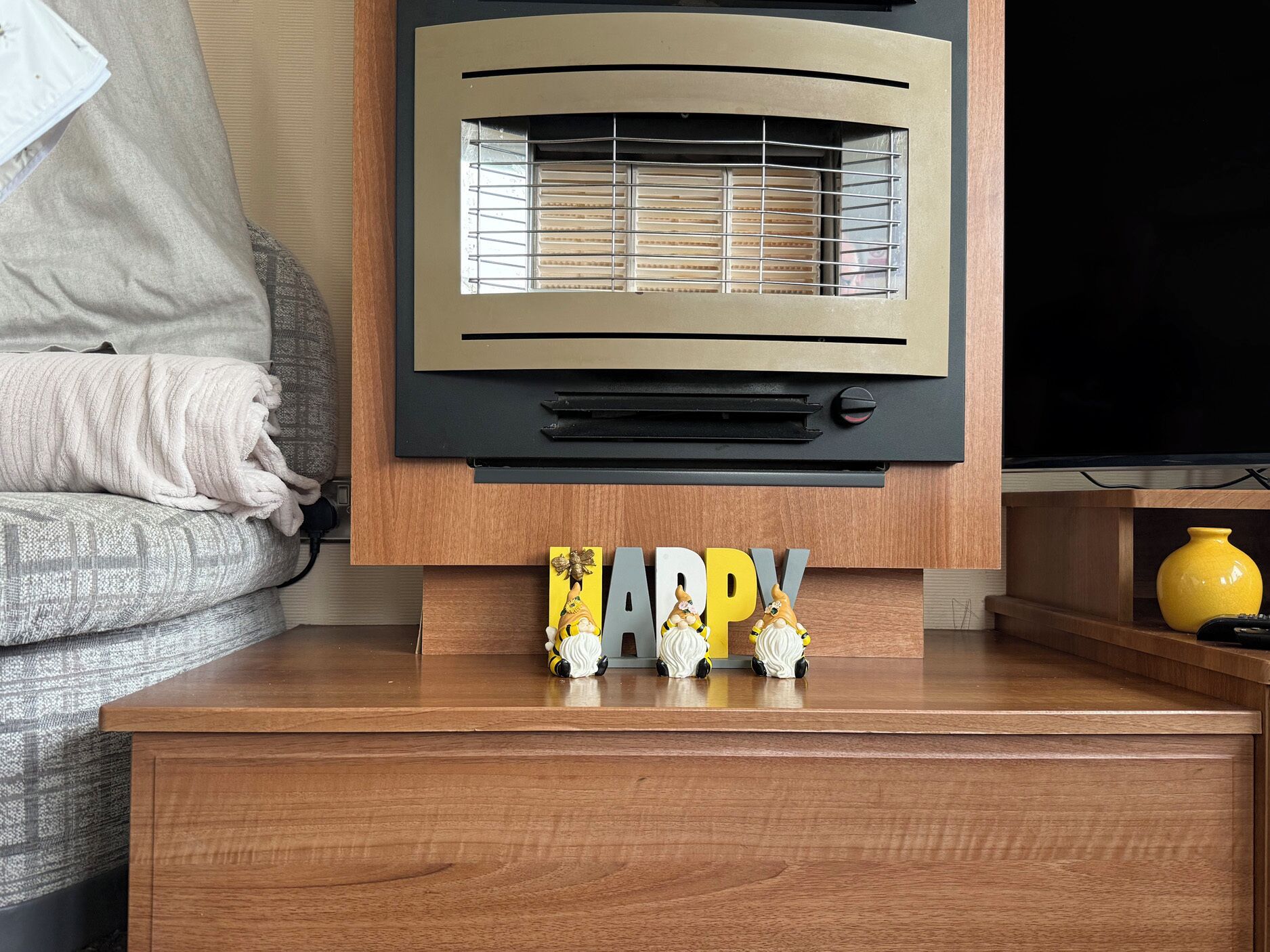 Ein modernes Wohnzimmer mit Couch, Fernseher, Holztisch und einem dekorativen 'HAPPY'-Schild mit Figuren.