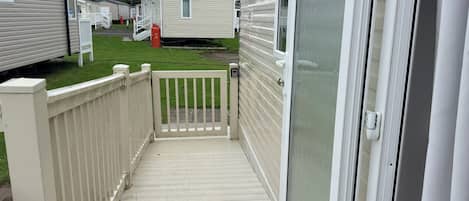 A narrow wooden deck leading to a mobile home with a screened door and a white railing.