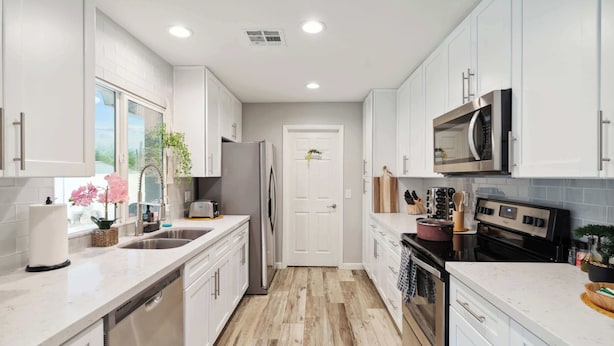 A modern kitchen with white cabinets, stainless steel appliances, and a herringbone wood floor. - Spacious, Pet friendly Scottsdale Retreat with Pool (Tempe)