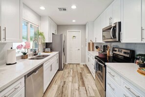 A modern kitchen with white cabinets, stainless steel appliances, and a herringbone wood floor. - Spacious, Pet friendly Scottsdale Retreat with Pool (Tempe)