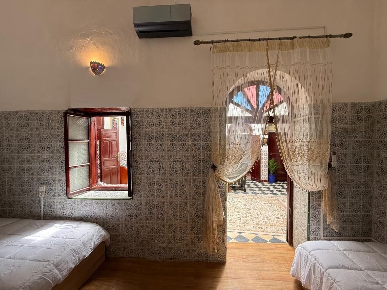 Ein Zimmer mit zwei Betten, einem Fenster mit Aussicht, einer Wand-Klimaanlage und einer Wand mit Muster.