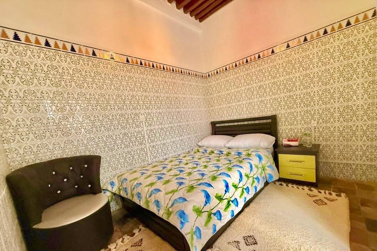 A bedroom with a bed, a chair, a nightstand, and patterned walls.