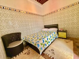 Un dormitorio con cama, una silla, una mesita de noche y paredes decoradas.
