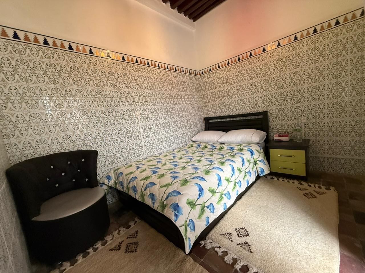 A bedroom with a bed, a chair, a nightstand, and patterned walls.