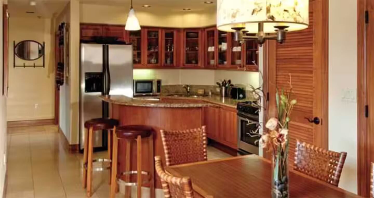 Een keuken met houten kastjes, een centraal eiland, barkrukken en een eettafel.