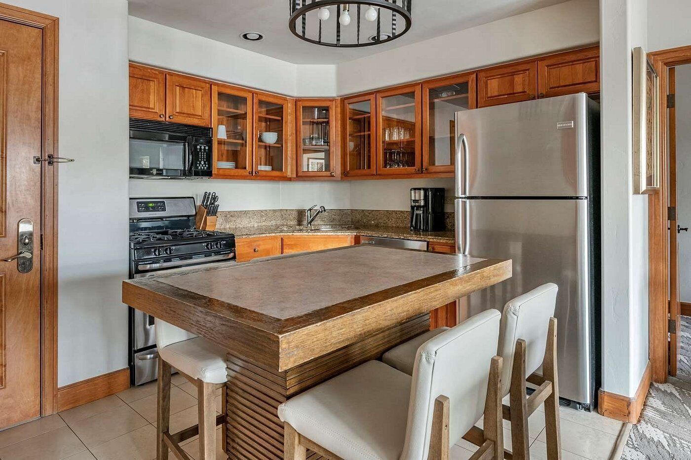 Una cocina con armarios de madera, un refrigerador de acero inoxidable, una isla integrada con taburetes de bar y una estufa a gas.