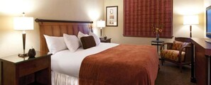 Ein Hotelzimmer mit einem großen Bett, zwei Nachttischen, einem Sessel, einem Schreibtisch und einem Fernseher.