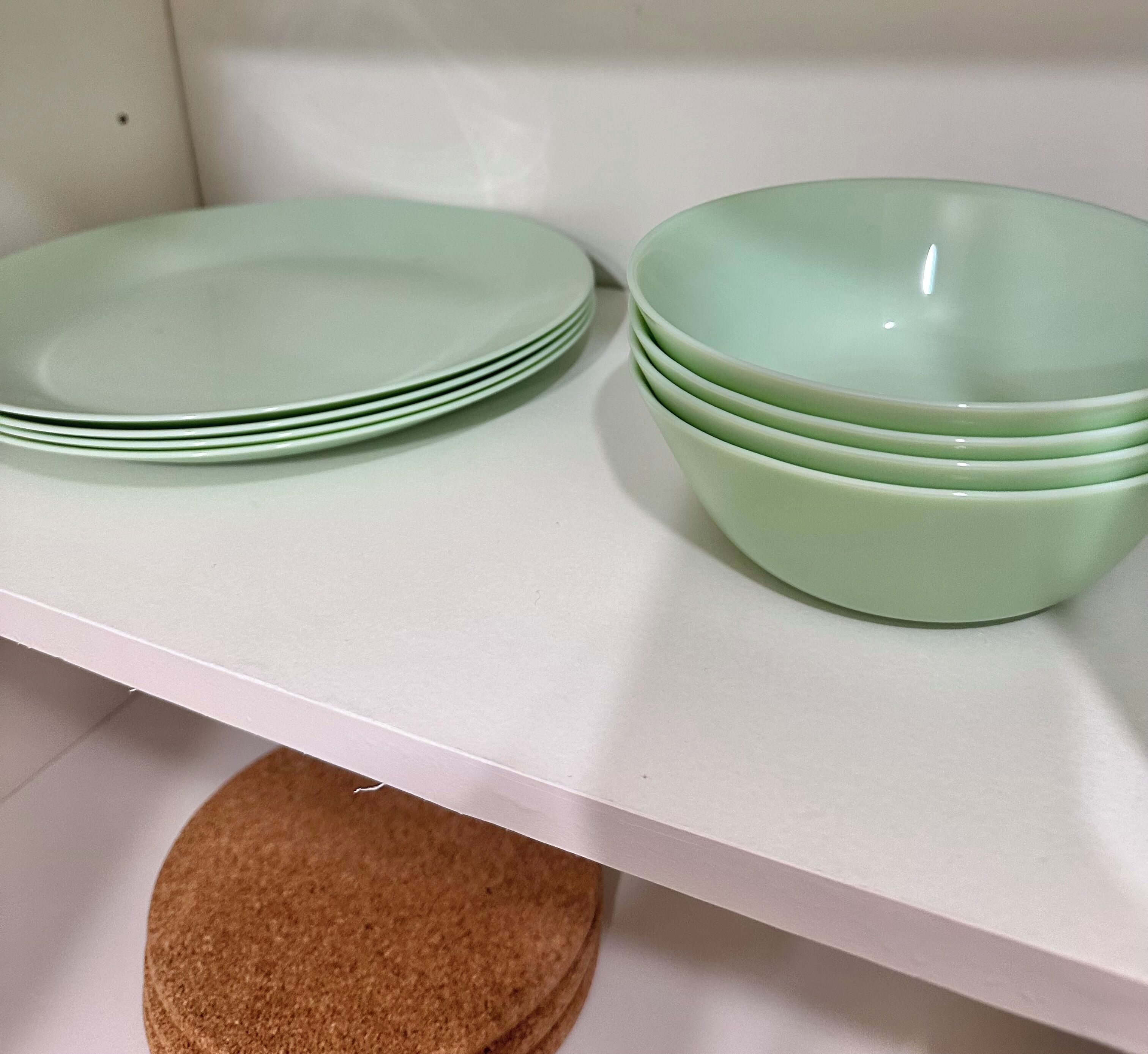 A white shelf with stacks of green plates and bowls.