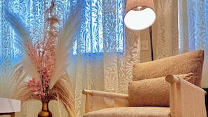 Ein gemütliches Zimmer mit einem gewebten Sessel, einer Vase mit Trockenblumen und einer Lampe.