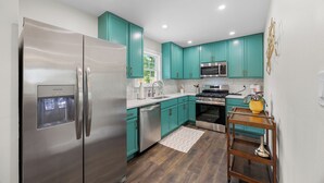 Una cocina moderna con armarios verde azulado, electrodomésticos de acero inoxidable y piso de madera.