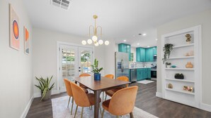 Una cocina moderna con gabinetes color turquesa, una isla central y un comedor con mesa de madera y sillas naranjas.