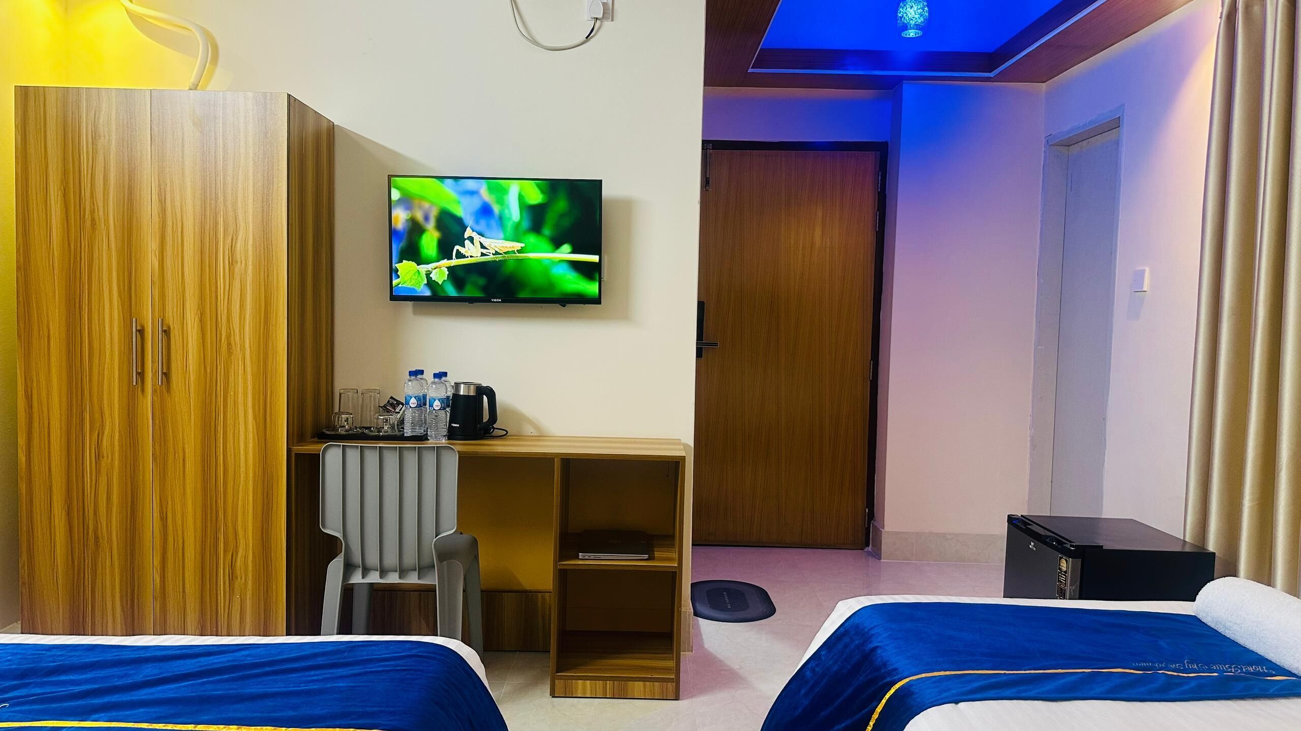 A hotel room with two beds, a desk with a chair, a television, and a wardrobe.