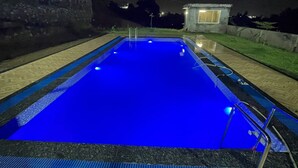 A rectangular swimming pool with a blue interior, surrounded by a tiled deck and a stone wall.