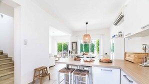 A modern kitchen with a central island, white cabinetry, and a view of greenery outside. - Villa Atlantis - Three Bedroom Villa, Sleeps 6 (Protaras)
