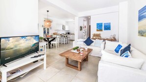 A modern living room with a flat-screen TV, a wooden coffee table, and a white sofa with blue pillows. - Villa Atlantis - Three Bedroom Villa, Sleeps 6 (Protaras)