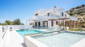 Une maison moderne à deux étages, dotée d’une piscine, d’un espace de détente extérieur et offrant une vue sur le paysage environnant.