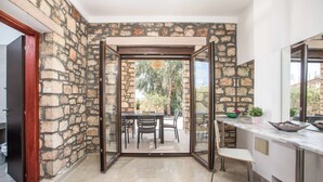 Une pièce aux murs en pierre, une porte vitrée donnant sur un espace extérieur avec une table et des chaises, et un comptoir de cuisine avec un saladier et une plante en pot.