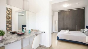 Une chambre moderne avec un grand lit, une armoire sombre, un plan de travail en marbre agrémenté de bols et une plante en pot.