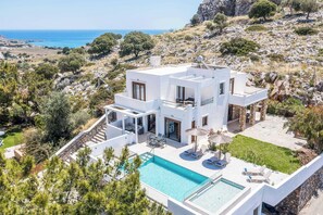 A modern villa with a swimming pool, outdoor seating, and a view of the sea.