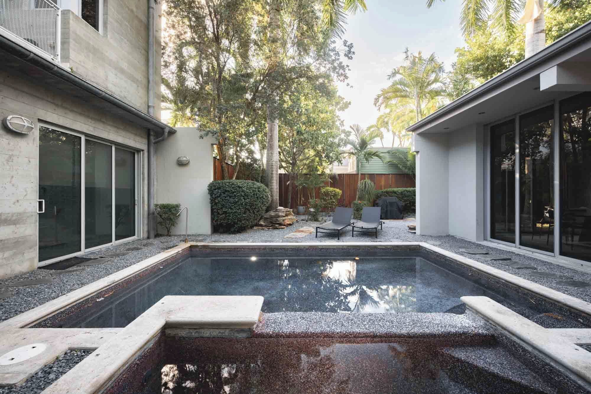 En moderne udendørs swimmingpool med stenkant, omgivet af en betonflisebelagt terrasse og et træhegn.