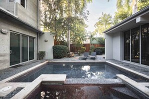 A modern outdoor swimming pool with a stone border, surrounded by a concrete deck and a wooden fence. - Contra House Key West (Key West)