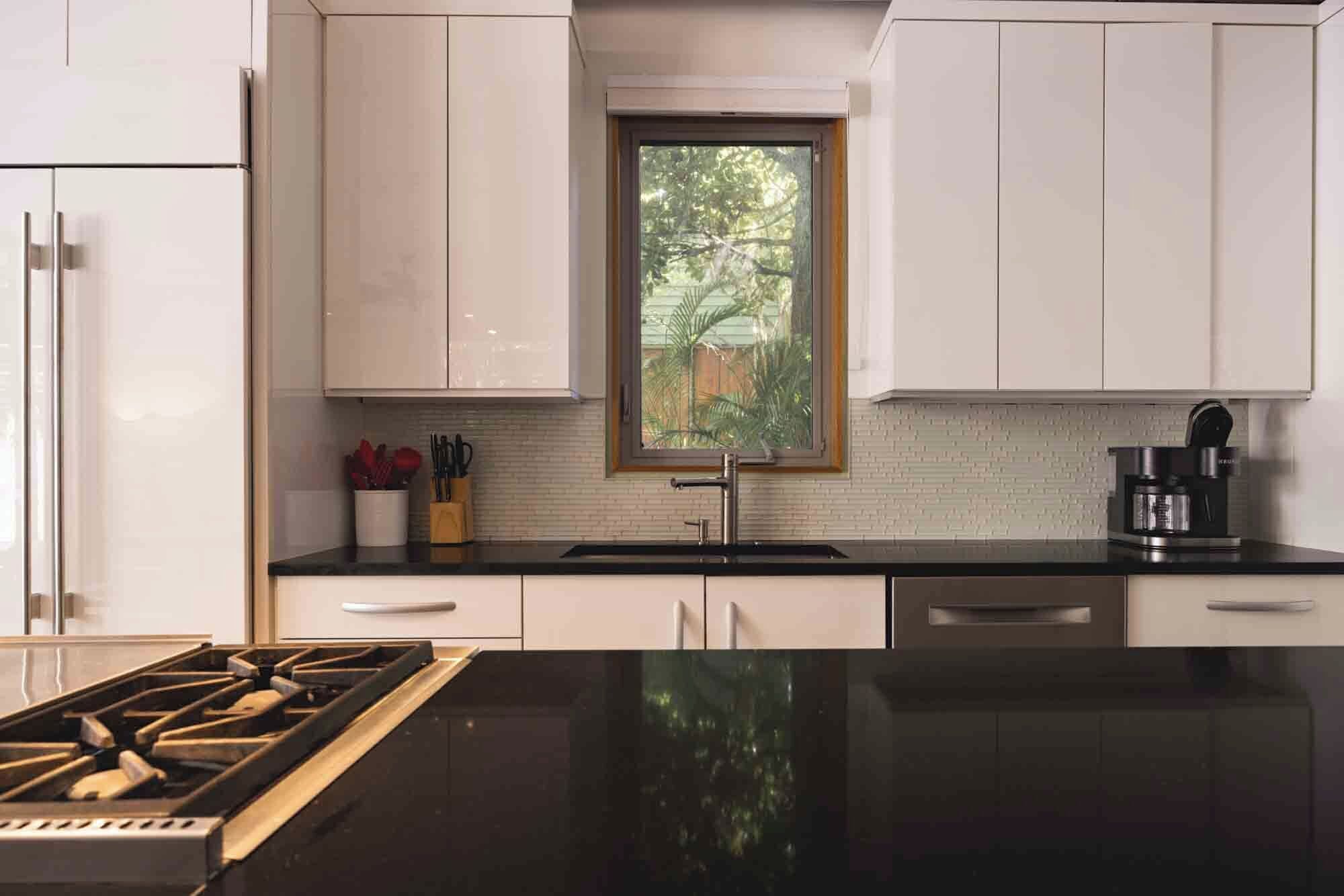 A modern kitchen with white cabinets, a black countertop, a stainless steel sink, and a coffee maker.