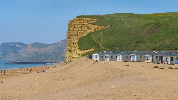 A coastal area with a sandy beach, a cliff, and a row of beach houses. - Freshwater Beach Holiday Park - Holiday Accommodation 17116 (Bridport)