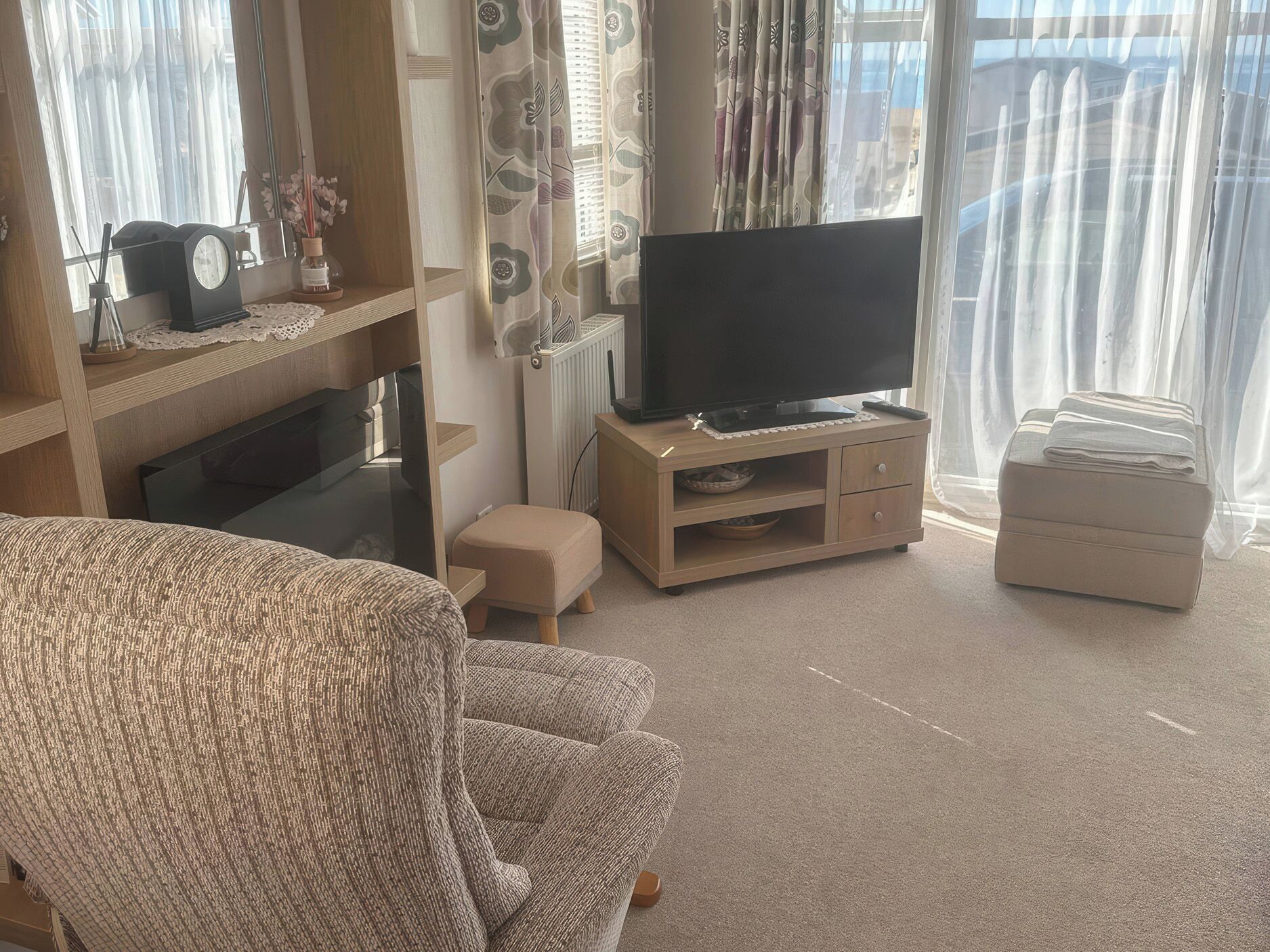A living room with a sofa, a television on a wooden stand, a small table with a clock, and a radiator.