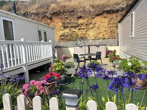 A residential backyard with a white deck, a patio table with chairs, and various potted plants and flowers. - Freshwater Beach Holiday Park - Holiday Accommodation 17116 (Bridport)