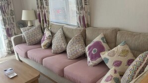 A cozy living area with a sofa set, patterned cushions, a small table, and a window with blinds. - Freshwater Beach Holiday Park - Holiday Accommodation 17116 (Bridport)