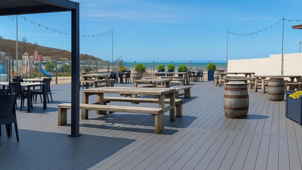Une terrasse extérieure avec des tables et des bancs en bois, des guirlandes lumineuses et des plantes en pot.