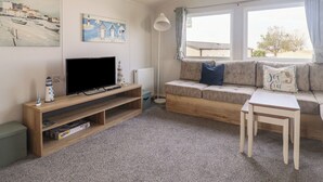 Un salon avec un téléviseur posé sur un meuble en bois, un canapé avec des coussins, une petite table et des œuvres d’art accrochées aux murs.