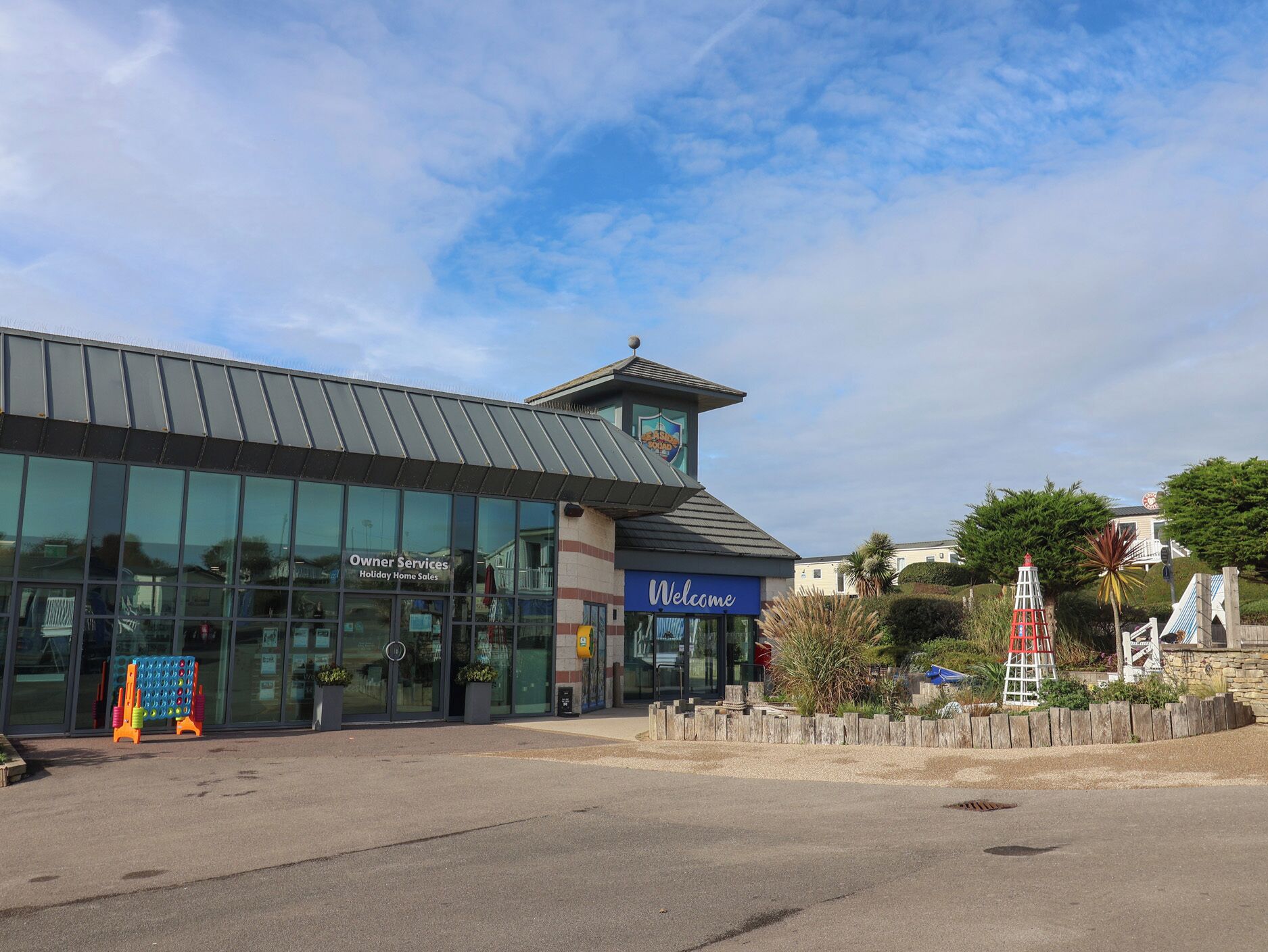 A building with a glass facade, a 'Welcome' sign, and a small tower with a clock.