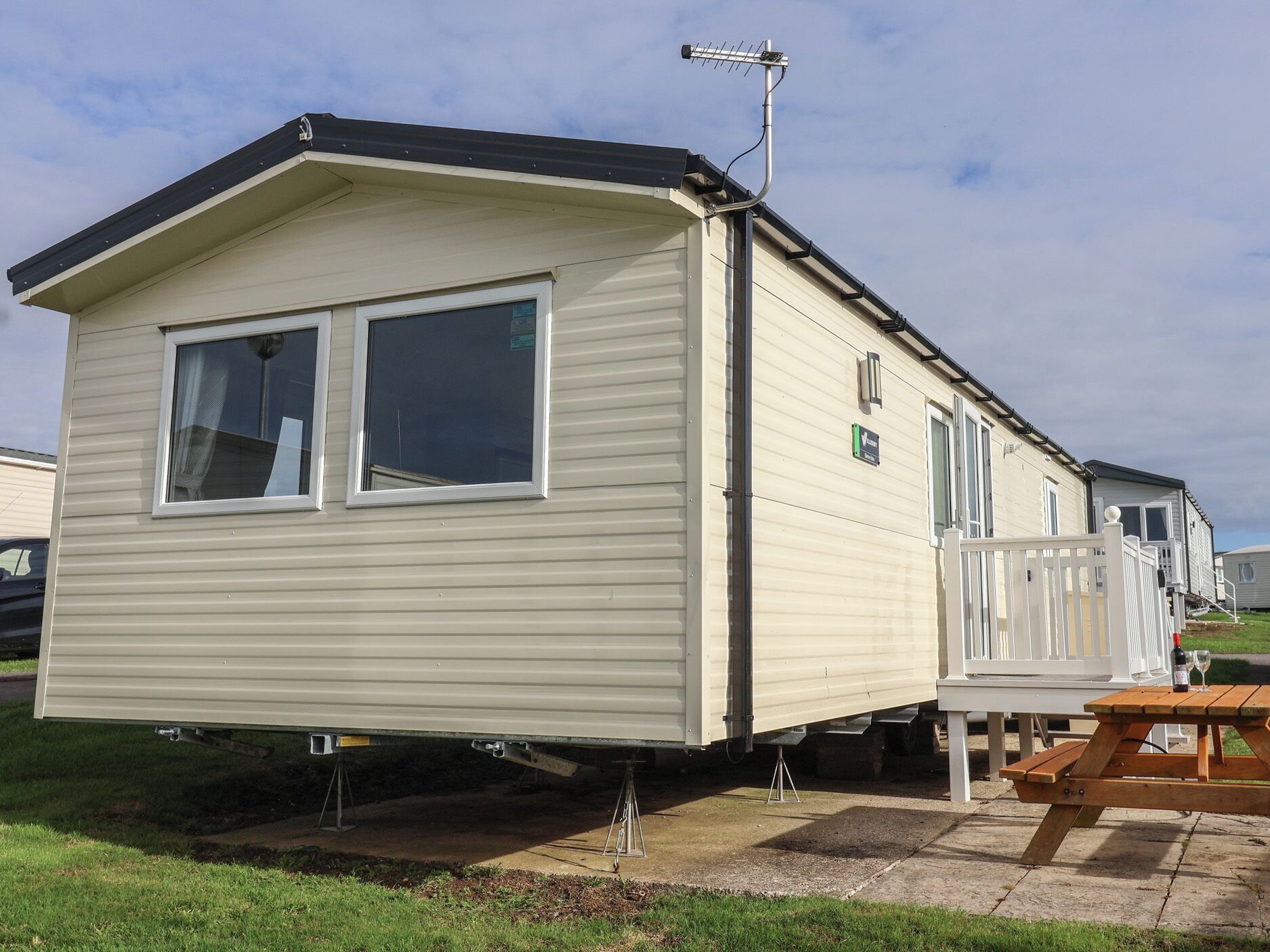 A single-story mobile home with a flat roof, a small porch with a white railing, and a satellite dish mounted on the roof.