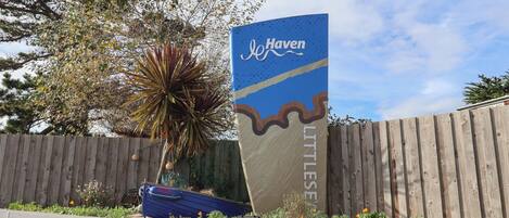 A sign for Haven Little Sea with a wooden fence and a plant in the foreground.