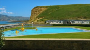 A swimming pool with inflatable toys, a stone wall, and a view of a lake and hills. - Freshwater Beach Holiday Park - Holiday Accommodation 12281 (Bridport)