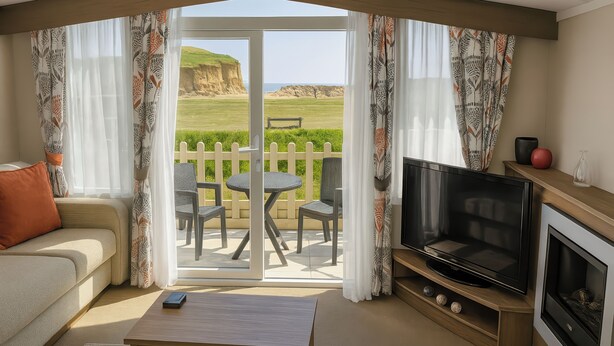 A living room with a sofa, coffee table, TV, and a view of a grassy area with a white picket fence. - Freshwater Beach Holiday Park - Holiday Accommodation 12281 (Bridport)